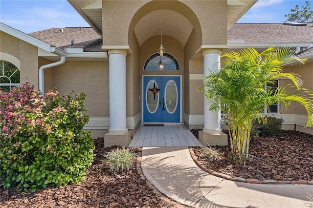 view of exterior entry with stucco siding and a shingled roof