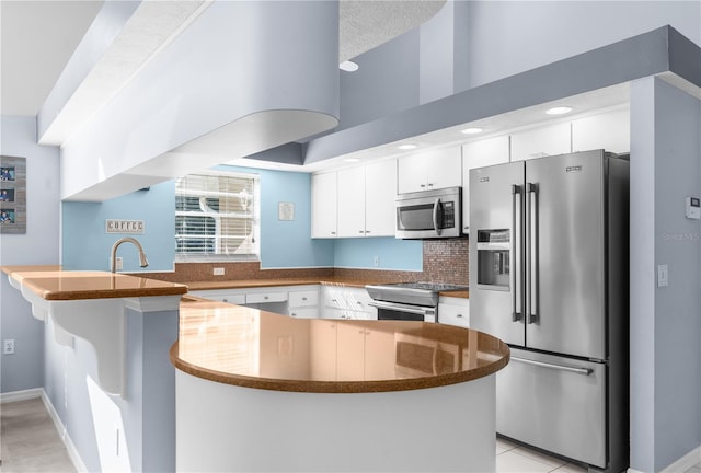 kitchen with stainless steel appliances, a peninsula, white cabinets, dark countertops, and tasteful backsplash