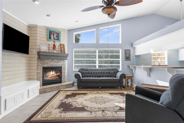 tiled living area with ceiling fan, a stone fireplace, high vaulted ceiling, and a sink