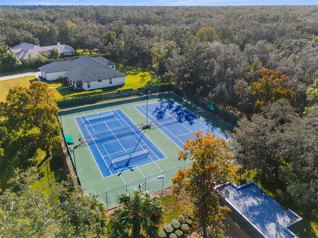 view of tennis court with a forest view and fence
