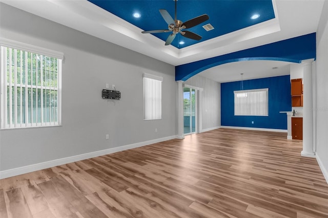 empty room with a tray ceiling, a ceiling fan, arched walkways, wood finished floors, and recessed lighting