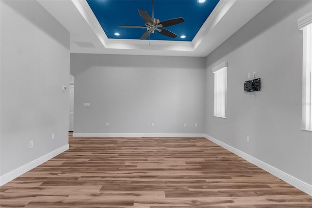 unfurnished room featuring ceiling fan, a tray ceiling, wood finished floors, baseboards, and ornamental molding