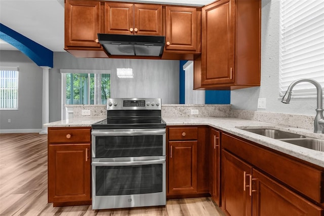 kitchen featuring double oven range, a sink, under cabinet range hood, light wood-style flooring, and light stone countertops
