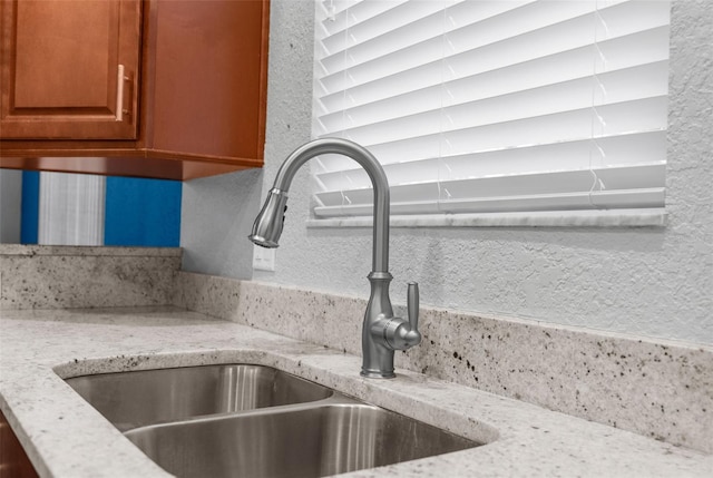 kitchen view of a sink, light stone countertops, and brown cabinetry