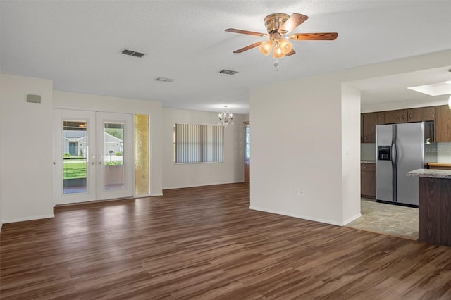 unfurnished living room featuring wood finished floors, a chandelier, ceiling fan, french doors, and baseboards