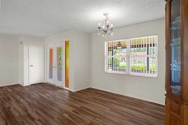 spare room featuring a chandelier, plenty of natural light, wood finished floors, and a textured ceiling