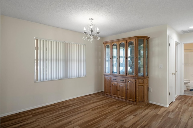 unfurnished dining area featuring wood finished floors, a chandelier, baseboards, and a textured ceiling