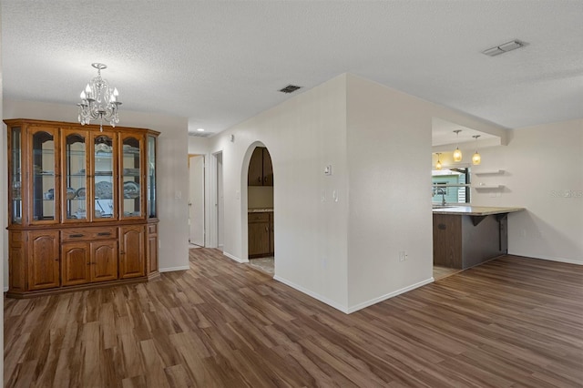 spare room with wood finished floors, arched walkways, a chandelier, baseboards, and a textured ceiling