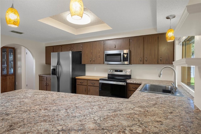 kitchen featuring appliances with stainless steel finishes, a sink, a tray ceiling, arched walkways, and pendant lighting
