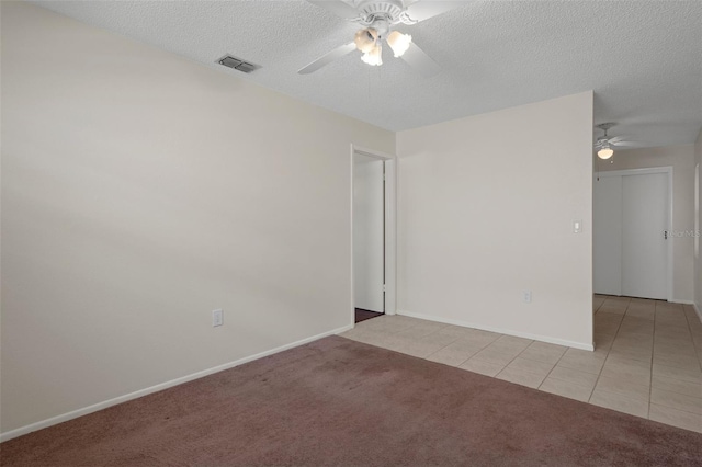 unfurnished room with ceiling fan, light tile patterned floors, a textured ceiling, light colored carpet, and baseboards