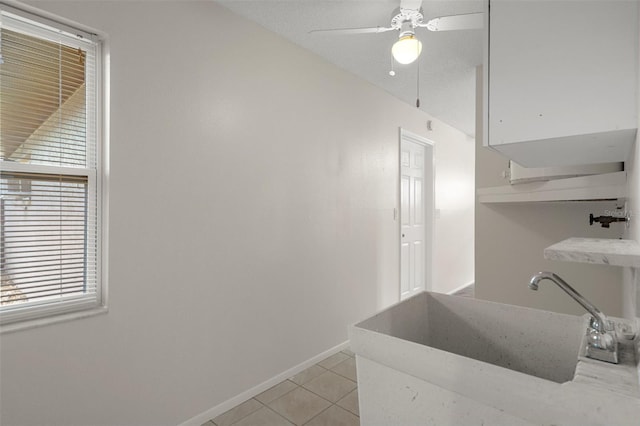kitchen featuring baseboards, light tile patterned floors, a sink, a ceiling fan, and white cabinetry
