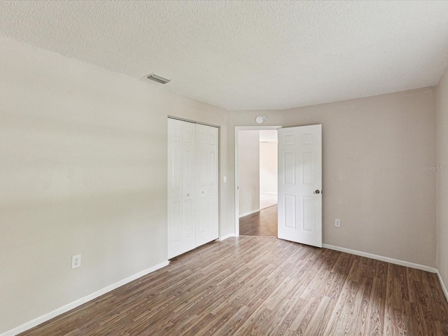 unfurnished bedroom with wood finished floors, baseboards, a closet, and a textured ceiling