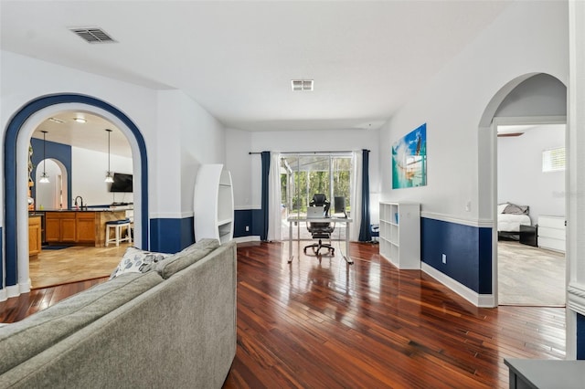 living area with arched walkways, hardwood / wood-style flooring, and baseboards