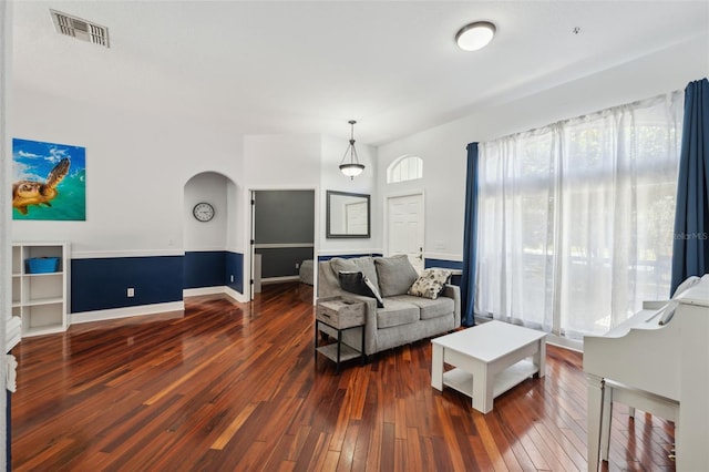 living area with dark wood-type flooring, arched walkways, and baseboards