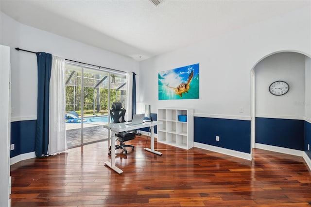 office space with baseboards, wood finished floors, and arched walkways