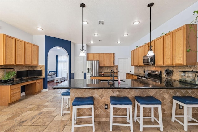 kitchen with stainless steel appliances, a peninsula, a sink, arched walkways, and dark countertops