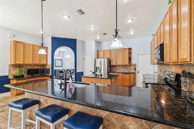 kitchen featuring stainless steel appliances, a sink, a peninsula, tasteful backsplash, and arched walkways