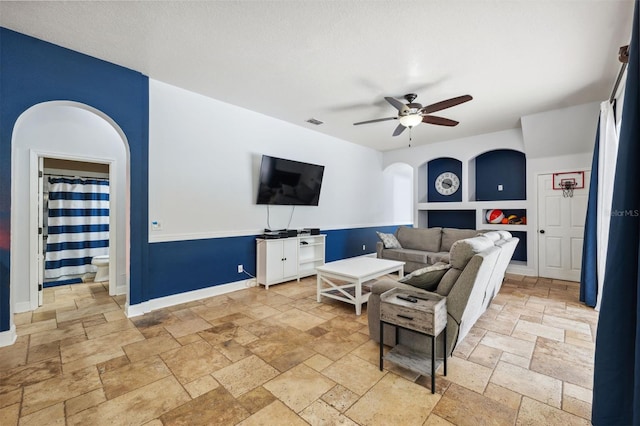 living room featuring stone tile floors, ceiling fan, and baseboards