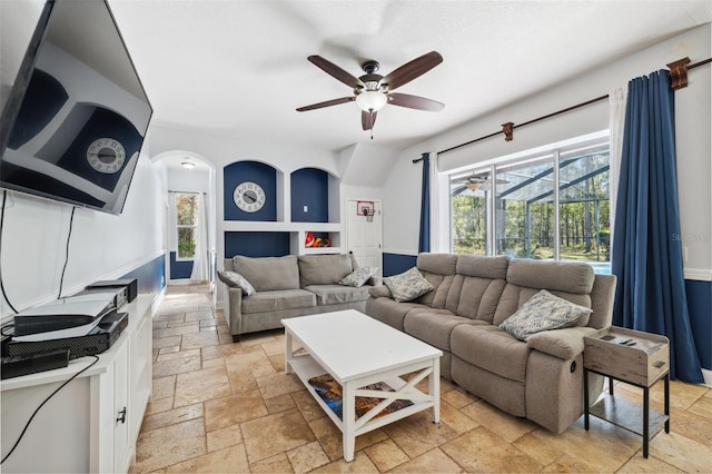 living room with stone tile floors, ceiling fan, and arched walkways
