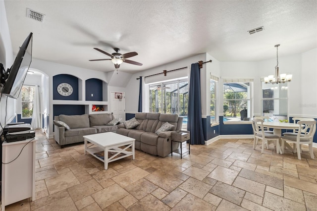 living room featuring stone tile flooring, a ceiling fan, a textured ceiling, a chandelier, and baseboards