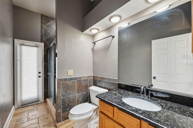 full bath with a shower stall, stone tile floors, vanity, toilet, and tile walls