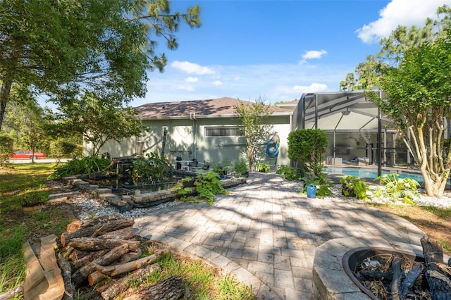 rear view of property with a patio, an outdoor pool, glass enclosure, stucco siding, and a fire pit