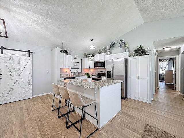 kitchen featuring appliances with stainless steel finishes, light wood-style floors, a kitchen island, a textured ceiling, and vaulted ceiling
