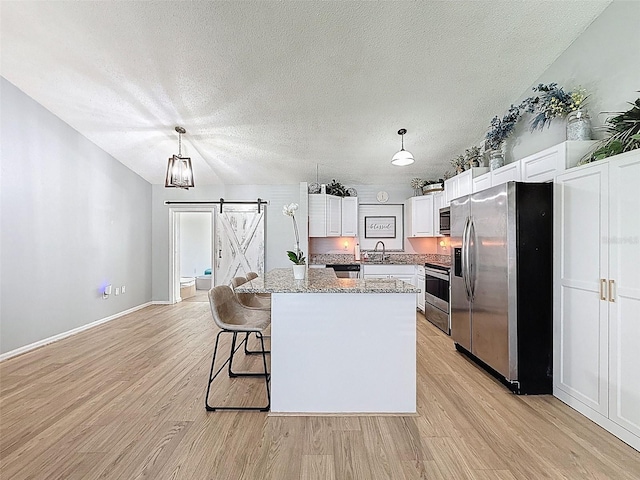 kitchen featuring appliances with stainless steel finishes, a barn door, light wood finished floors, white cabinets, and a textured ceiling
