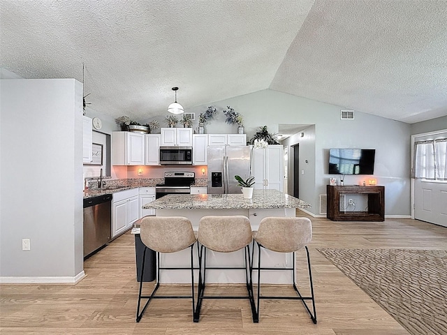 kitchen with appliances with stainless steel finishes, a sink, vaulted ceiling, a kitchen island, and light wood-style flooring