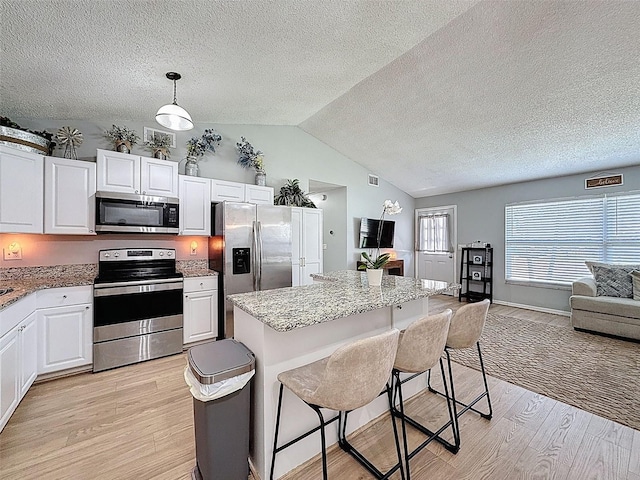 kitchen with appliances with stainless steel finishes, light wood finished floors, lofted ceiling, a textured ceiling, and open floor plan