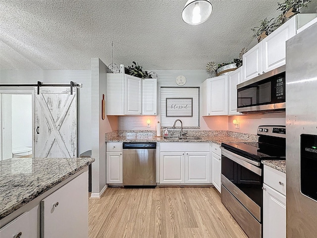 kitchen featuring appliances with stainless steel finishes, a textured ceiling, a sink, light wood finished floors, and white cabinetry