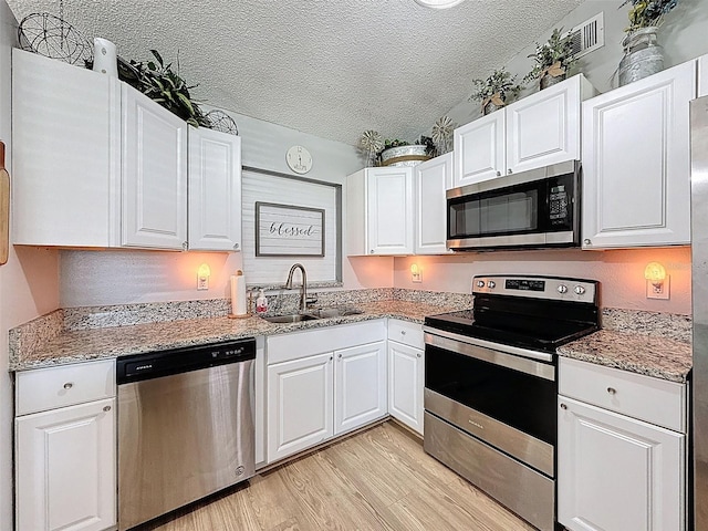 kitchen with appliances with stainless steel finishes, a sink, a textured ceiling, white cabinets, and light wood-type flooring