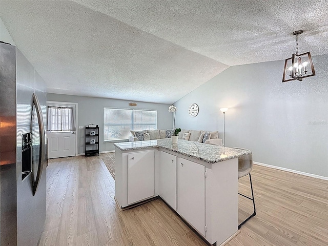 kitchen with stainless steel fridge, a textured ceiling, open floor plan, light wood-type flooring, and baseboards