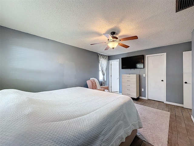 bedroom featuring wood finished floors, baseboards, ceiling fan, a textured ceiling, and multiple closets