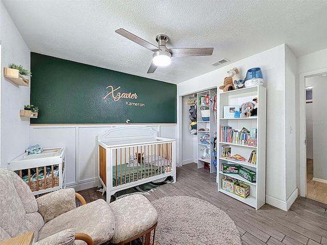 bedroom featuring a textured ceiling, wood finished floors, a decorative wall, wainscoting, and a closet