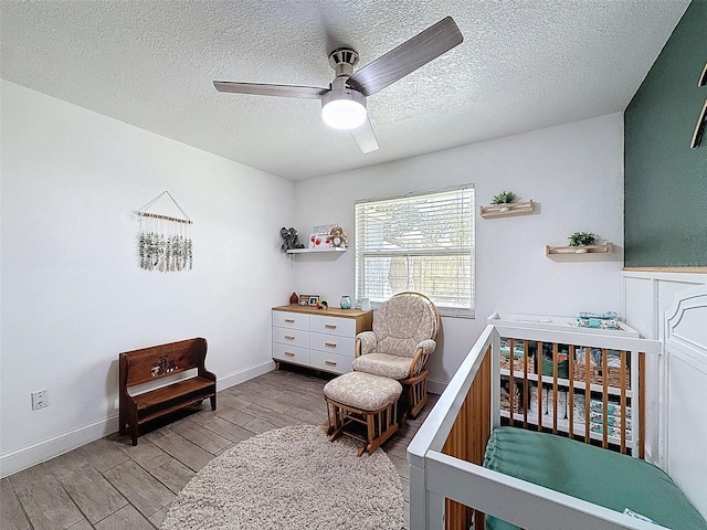 bedroom with wood finished floors, a nursery area, a textured ceiling, a ceiling fan, and baseboards