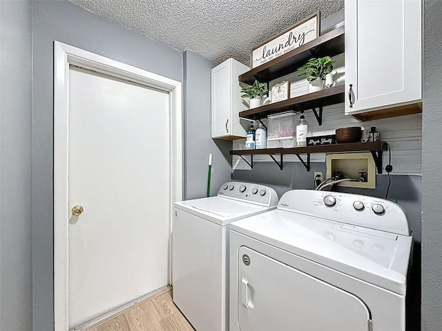 clothes washing area featuring cabinet space, washing machine and clothes dryer, light wood-style flooring, and a textured ceiling
