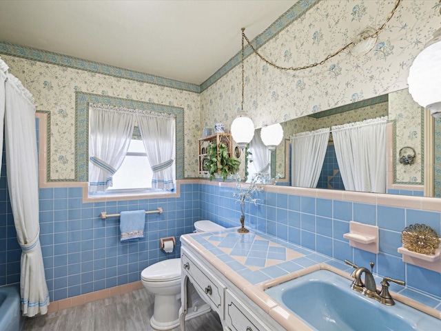 6823 Oak Hill Dr, New Port Richey, FL 34653 - full bathroom featuring tile walls, toilet, wood finished floors, wainscoting, and wallpapered walls