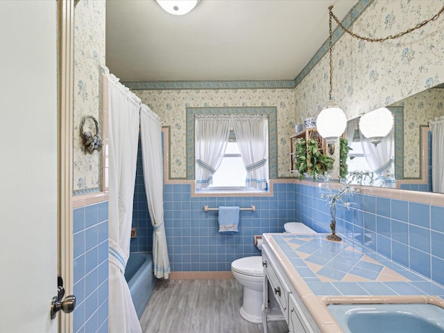 6823 Oak Hill Dr, New Port Richey, FL 34653 - bathroom featuring wallpapered walls, wainscoting, toilet, tile walls, and wood finished floors
