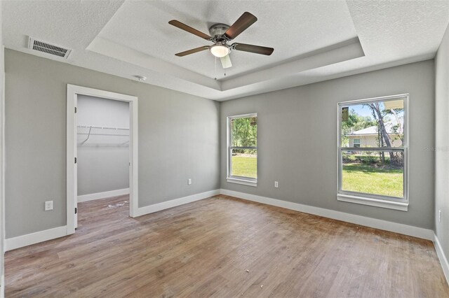 8792 N Sandree Dr, Dunnellon, FL 34434 - unfurnished bedroom featuring a tray ceiling, multiple windows, light wood finished floors, baseboards, and a textured ceiling