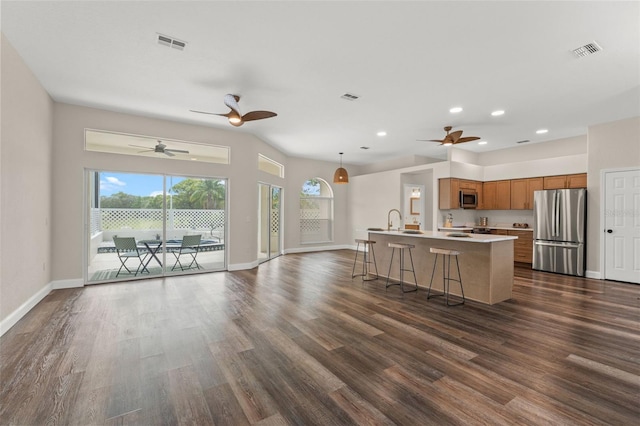 kitchen with appliances with stainless steel finishes, brown cabinetry, open floor plan, dark wood-type flooring, and a ceiling fan