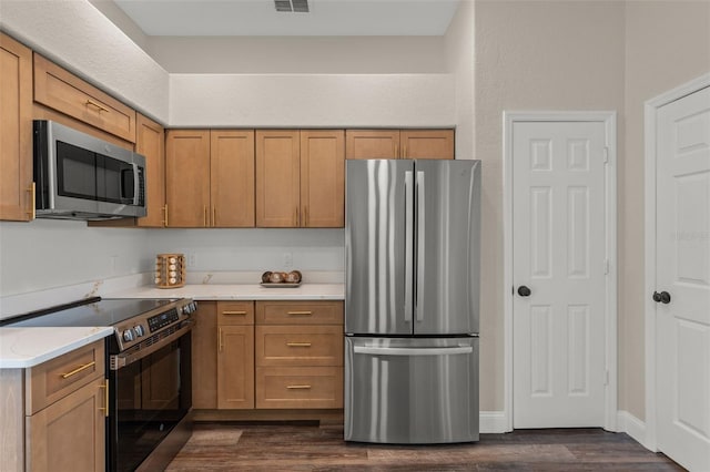 kitchen with appliances with stainless steel finishes, dark wood-style flooring, light countertops, and brown cabinetry