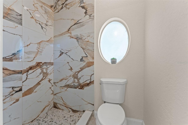 bathroom featuring a marble finish shower and toilet