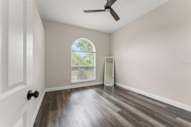 spare room with dark wood-style flooring, a ceiling fan, and baseboards