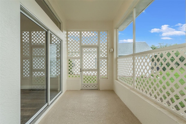 unfurnished sunroom featuring plenty of natural light, a textured wall, and carpet floors