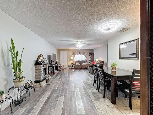 6213 Emerson Dr, New Port Richey, FL 34653 - dining room featuring light wood-style flooring, ceiling fan, a textured ceiling, and a fireplace