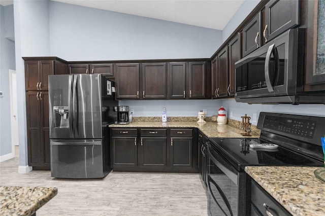 kitchen with appliances with stainless steel finishes, vaulted ceiling, light wood finished floors, light stone countertops, and dark brown cabinets