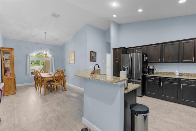 kitchen with stainless steel fridge, baseboards, light wood finished floors, light stone counters, and high vaulted ceiling