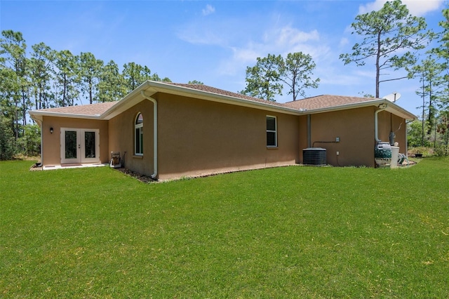 rear view of property with french doors, stucco siding, central air condition unit, and a lawn