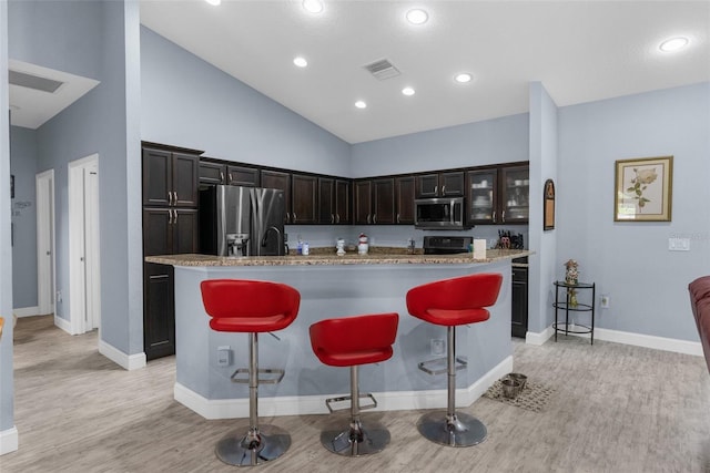 kitchen featuring stainless steel appliances, light wood-style flooring, a kitchen breakfast bar, baseboards, and recessed lighting